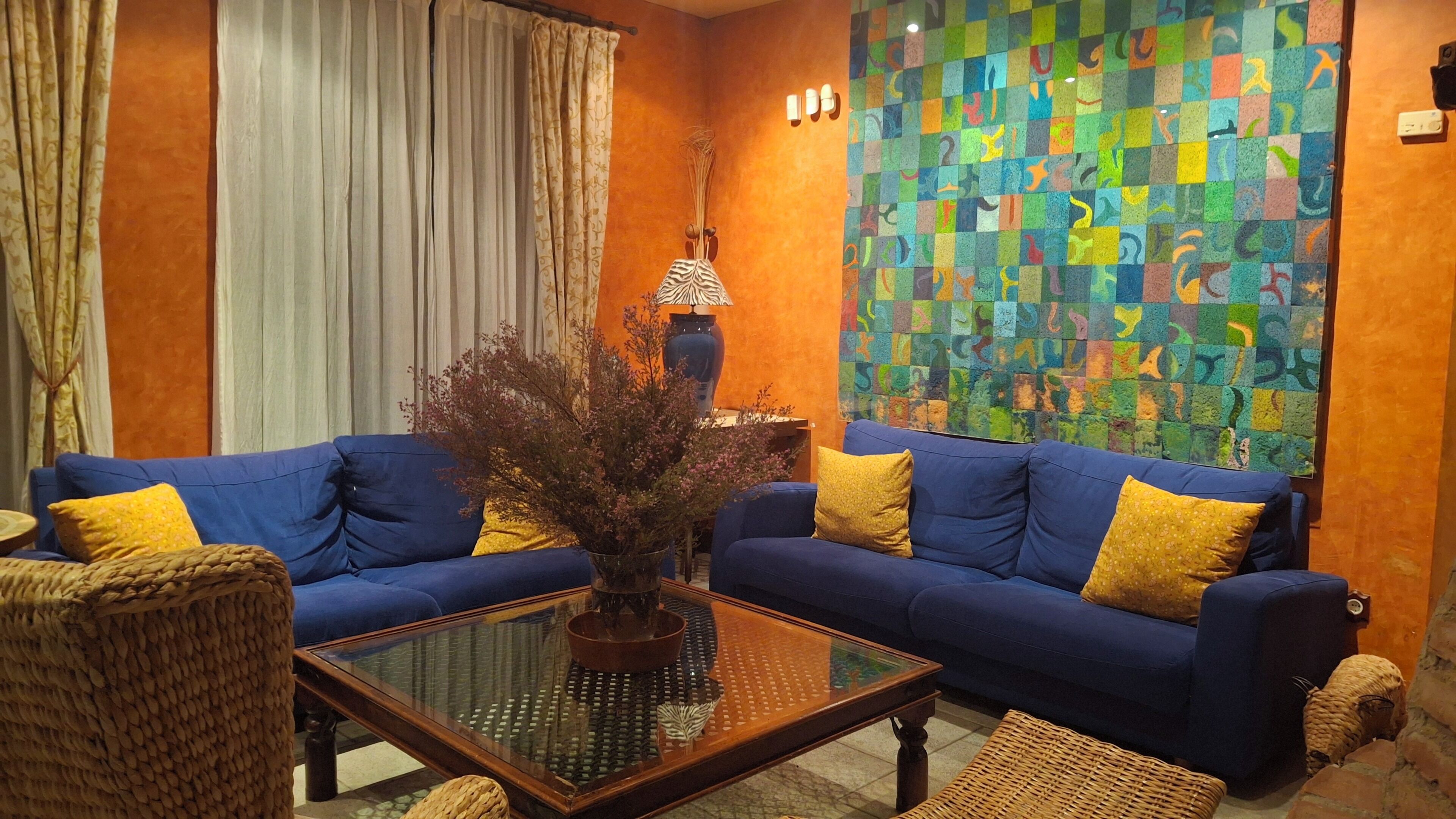 A living room with two blue sofas, a glass coffee table, and a colorful abstract wall art.