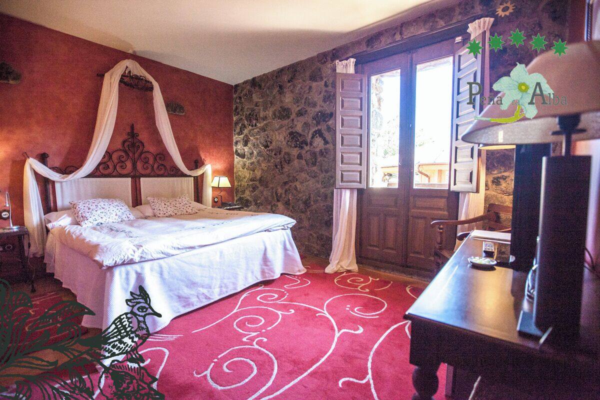 A bedroom with a four-poster bed, a stone wall, a red carpet, and a wooden desk with a lamp.