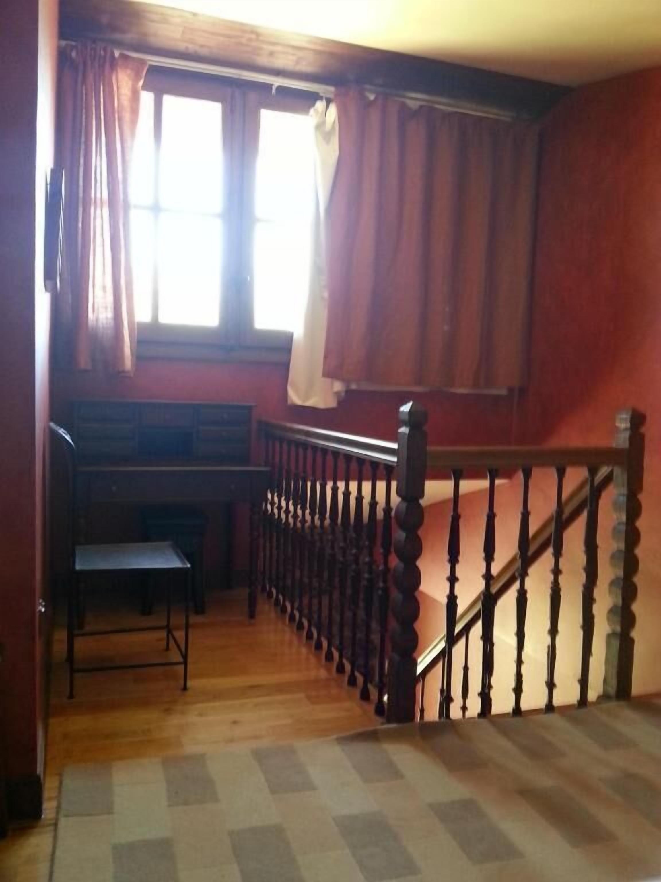 Een kamer met een houten trap, een bureau en een raam met gordijnen.