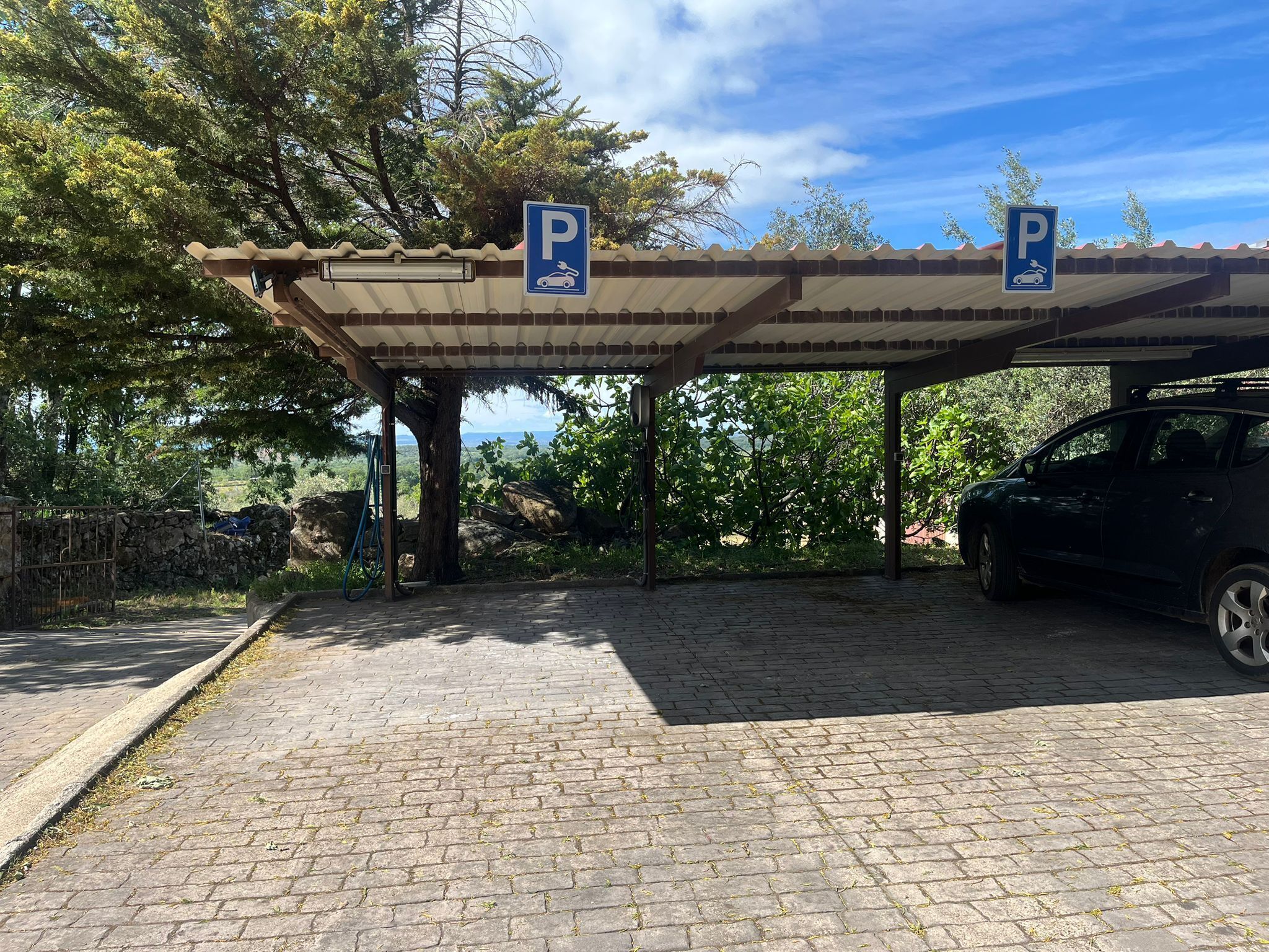 Un área de estacionamiento techada con dos letreros de estacionamiento, un camino pavimentado y un automóvil bajo la protección.