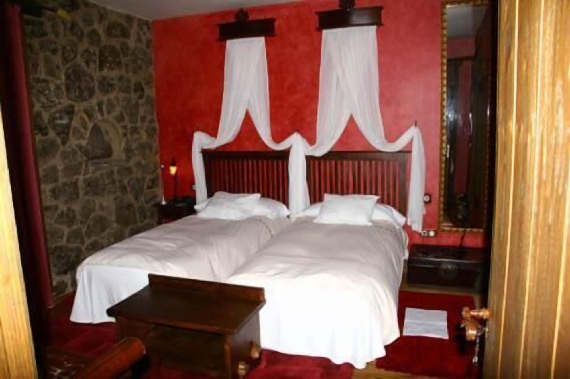 A double bed with white linens, a wooden headboard, and a stone wall.