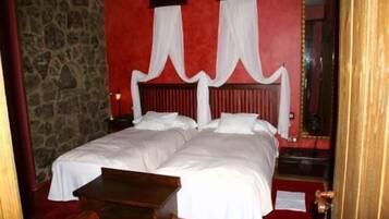 A double bed with white linens, a wooden headboard, and a stone wall.