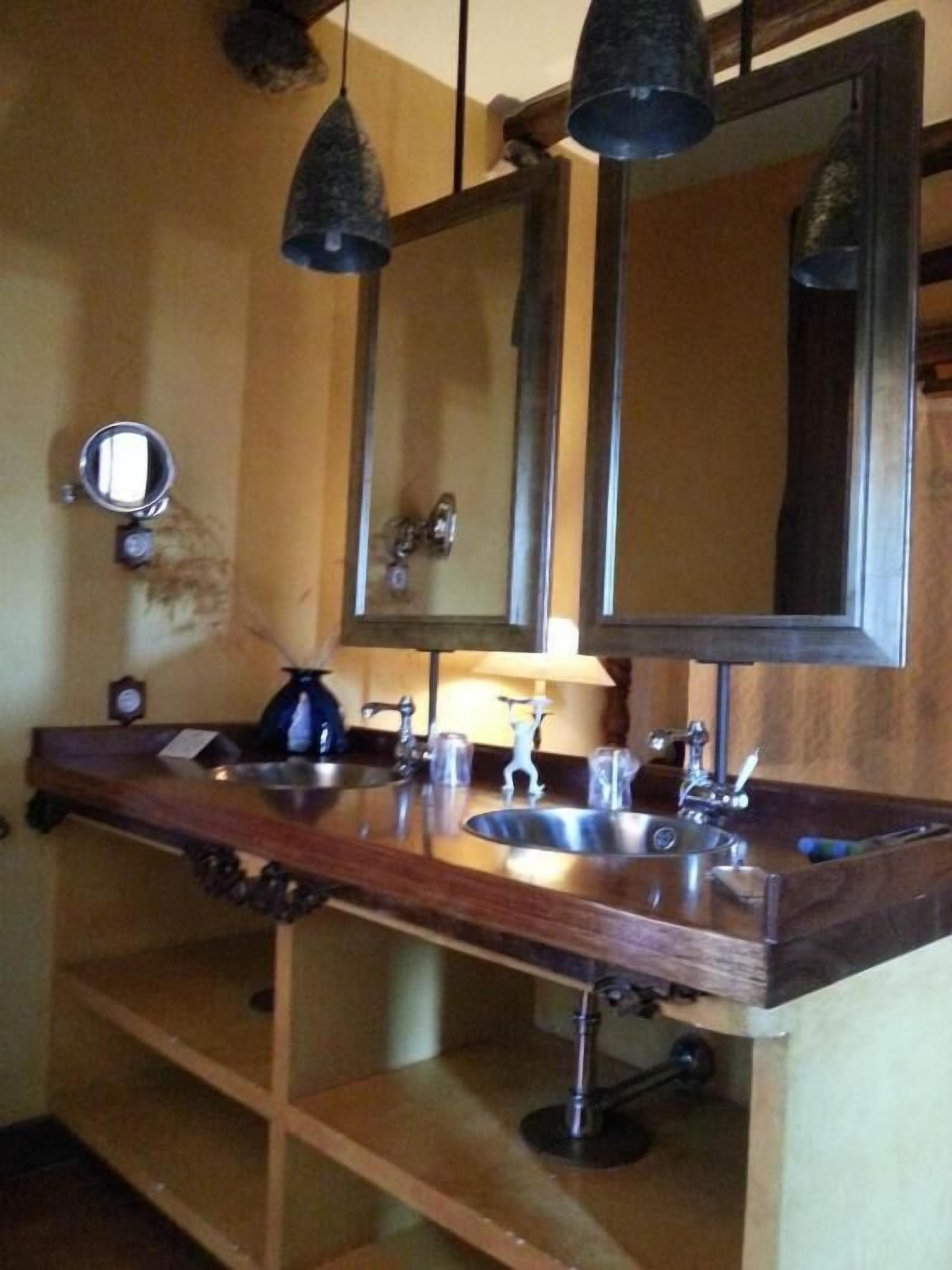 A bathroom with a wooden vanity, two sinks, a mirror, and hanging pendant lights.
