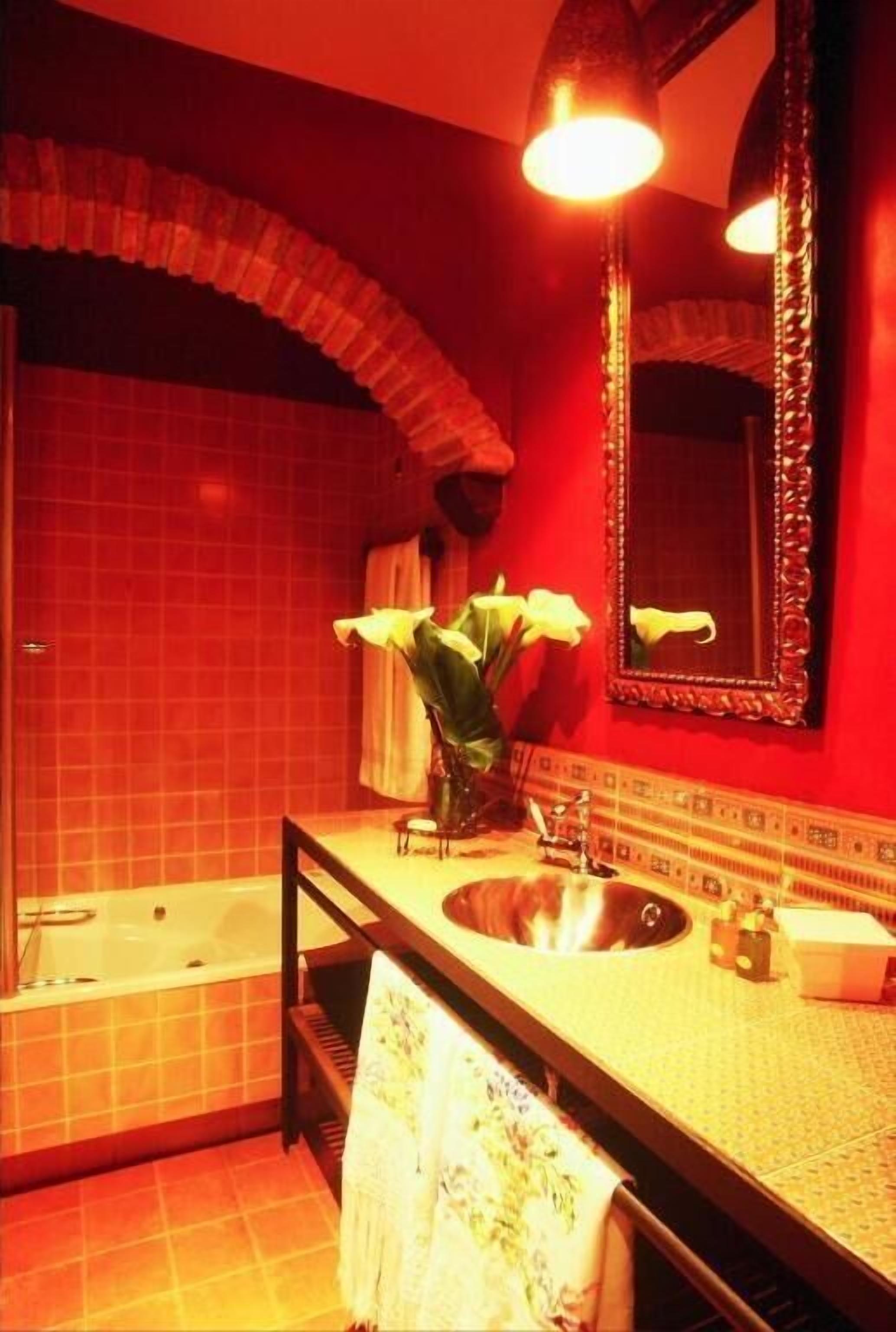 A bathroom with a bathtub, a sink, a mirror, and a vase with flowers.