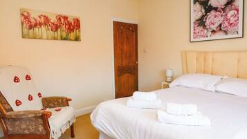 A bedroom with a bed, a chair, a door, and two paintings on the walls.