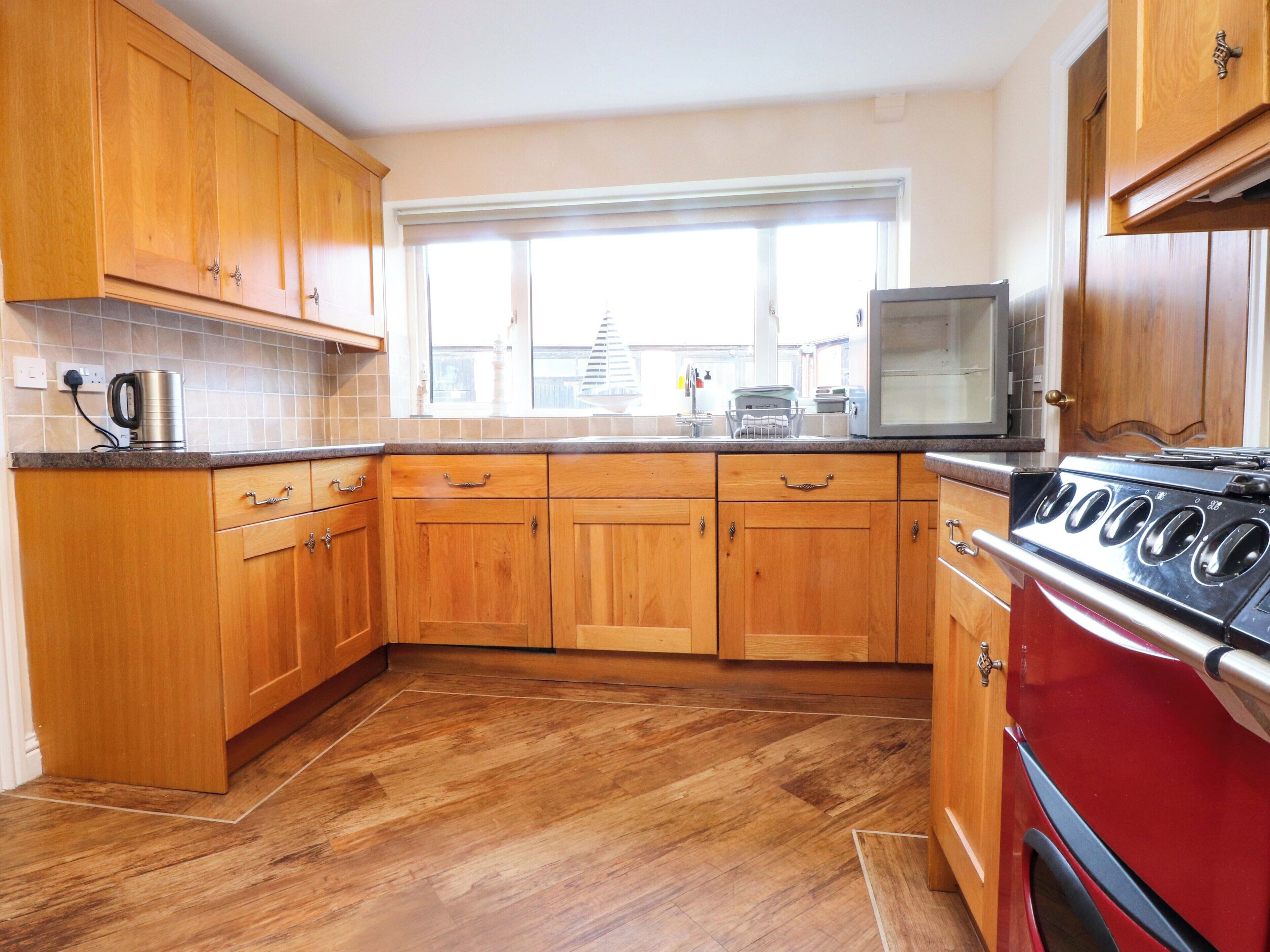 A kitchen with wooden cabinets, a red stove, and a window with blinds.