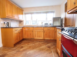 Una cocina con armarios de madera, una estufa roja y una ventana con persianas.