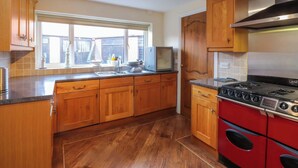 A kitchen with wooden cabinets, a red stove, a microwave, and a window with a view. - The Old Stables (Colwyn Bay)