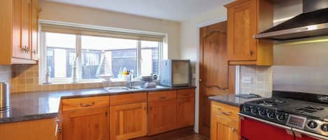 A kitchen with wooden cabinets, a red stove, a microwave, and a window with a view.