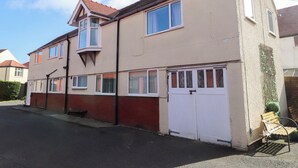 A two-story residential building with a red brick facade, multiple windows, a satellite dish, and a gated driveway. - The Old Stables (Colwyn Bay)