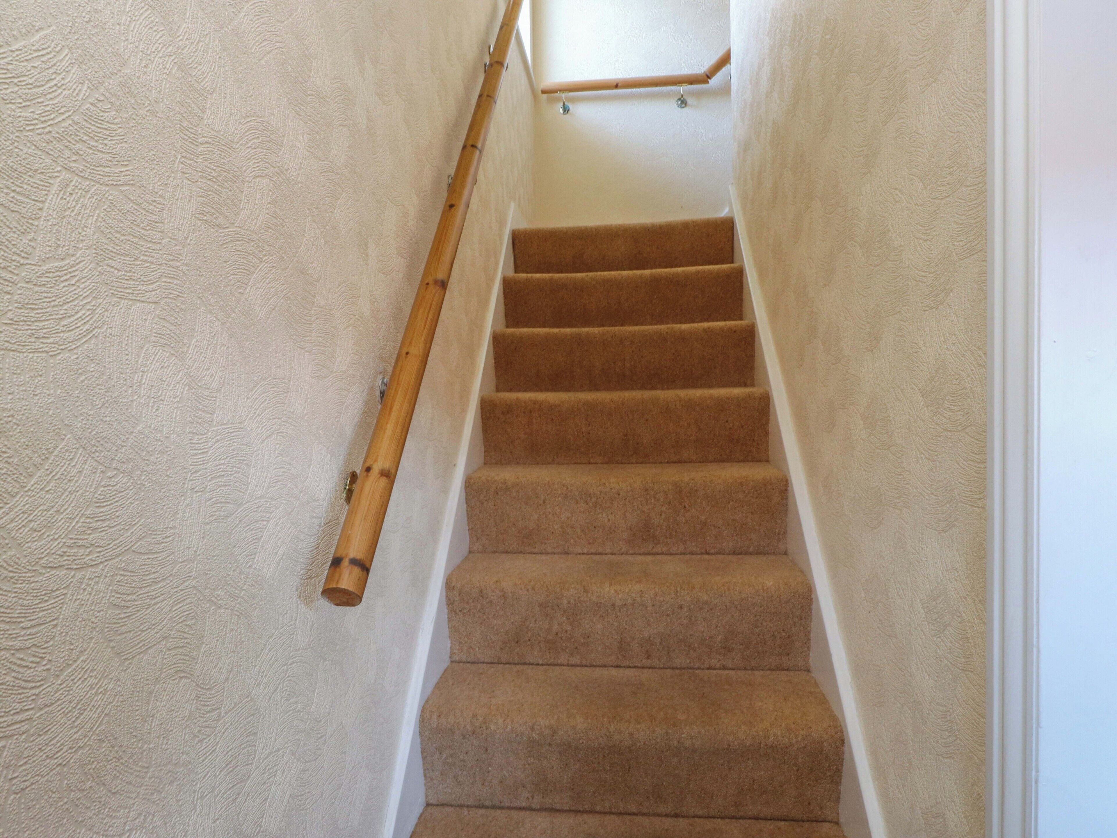 A carpeted staircase with a wooden handrail and a white textured wall.