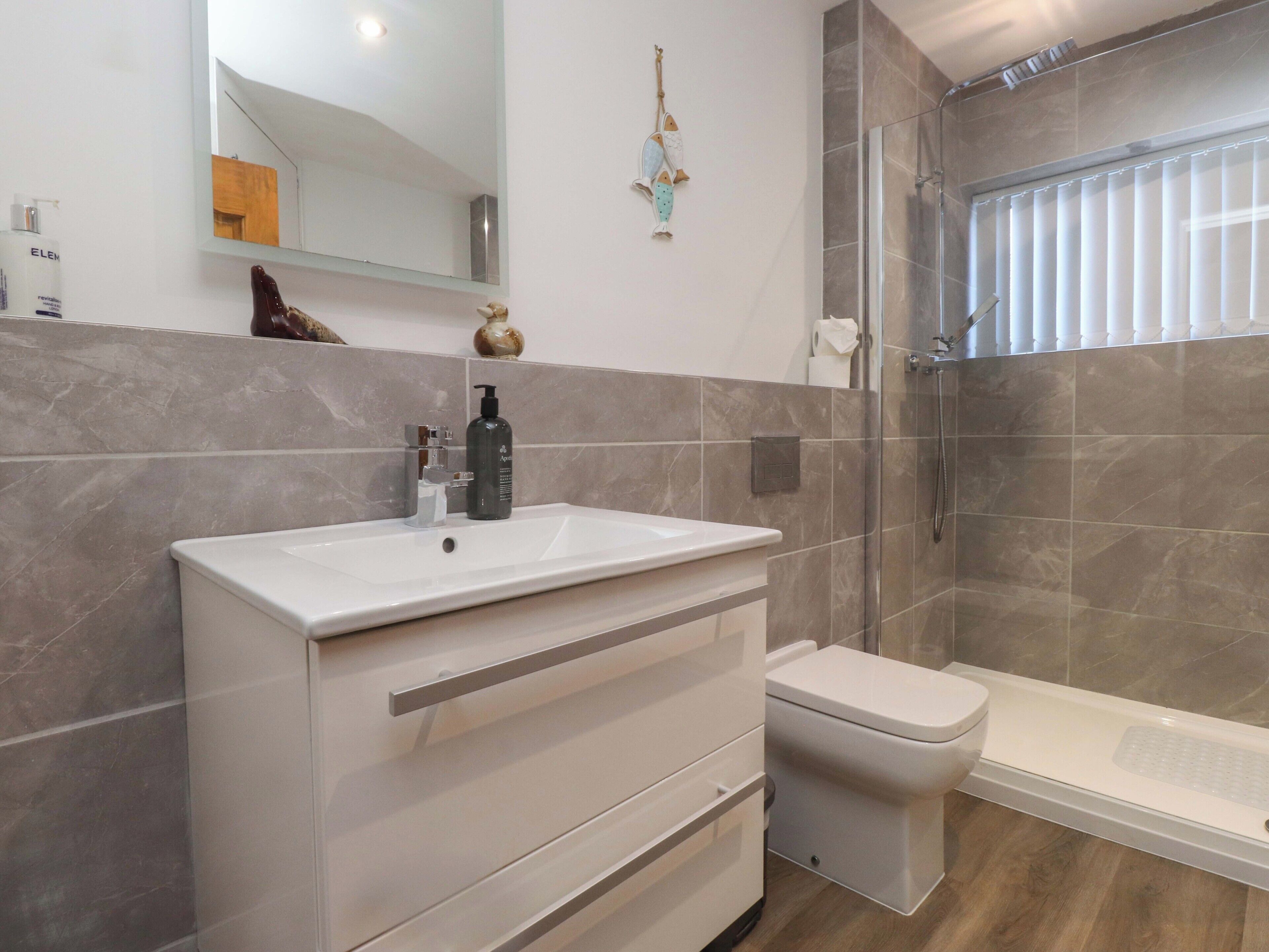 Ein modernes Badezimmer mit einem weißen Waschtisch, einer Duschkabine und einer marmorverkleideten Wand.