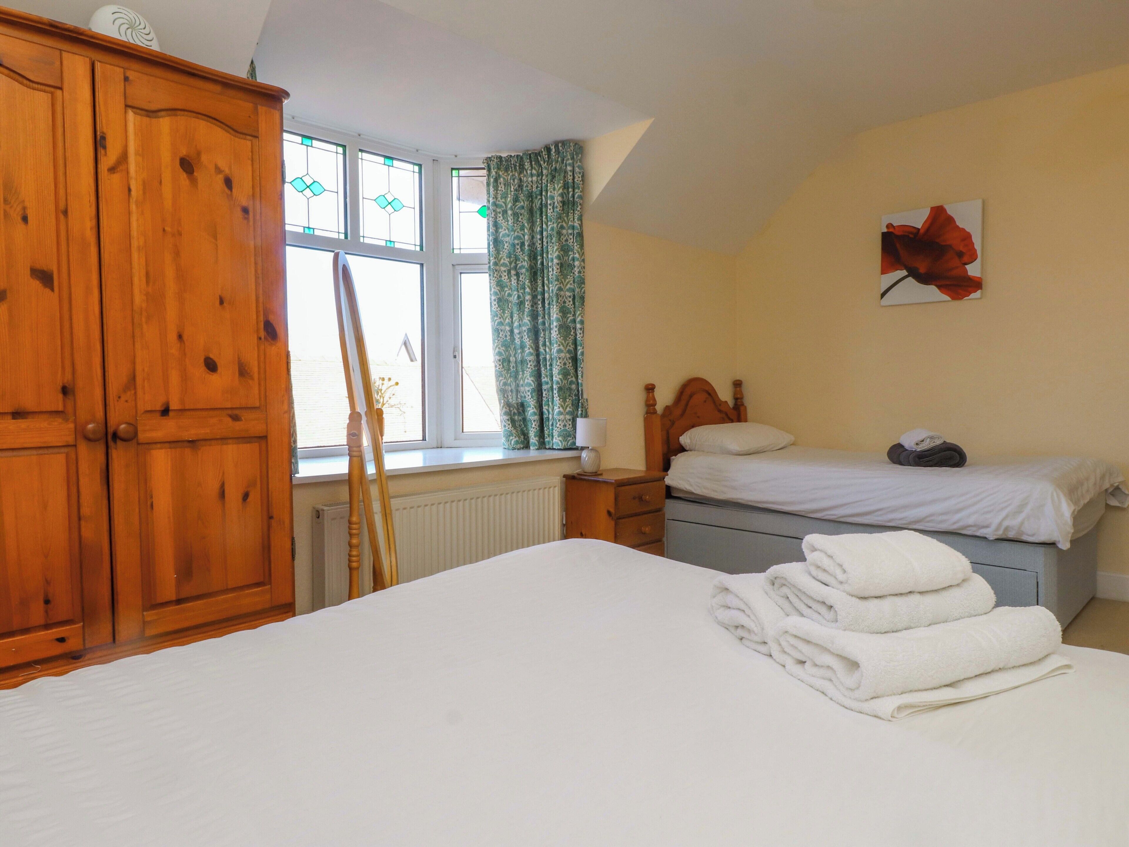 A bedroom with a large bed, a smaller bed, wooden wardrobe, a radiator, a window with curtains, and a painting on the wall.