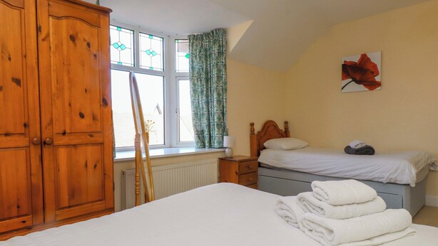 A bedroom with a large bed, a smaller bed, wooden wardrobe, a radiator, a window with curtains, and a painting on the wall. - The Old Stables (Colwyn Bay)