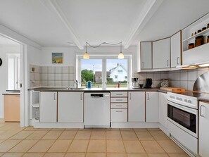 Une cuisine moderne avec des meubles blancs, une grande fenêtre et une vue sur une maison à l’extérieur.