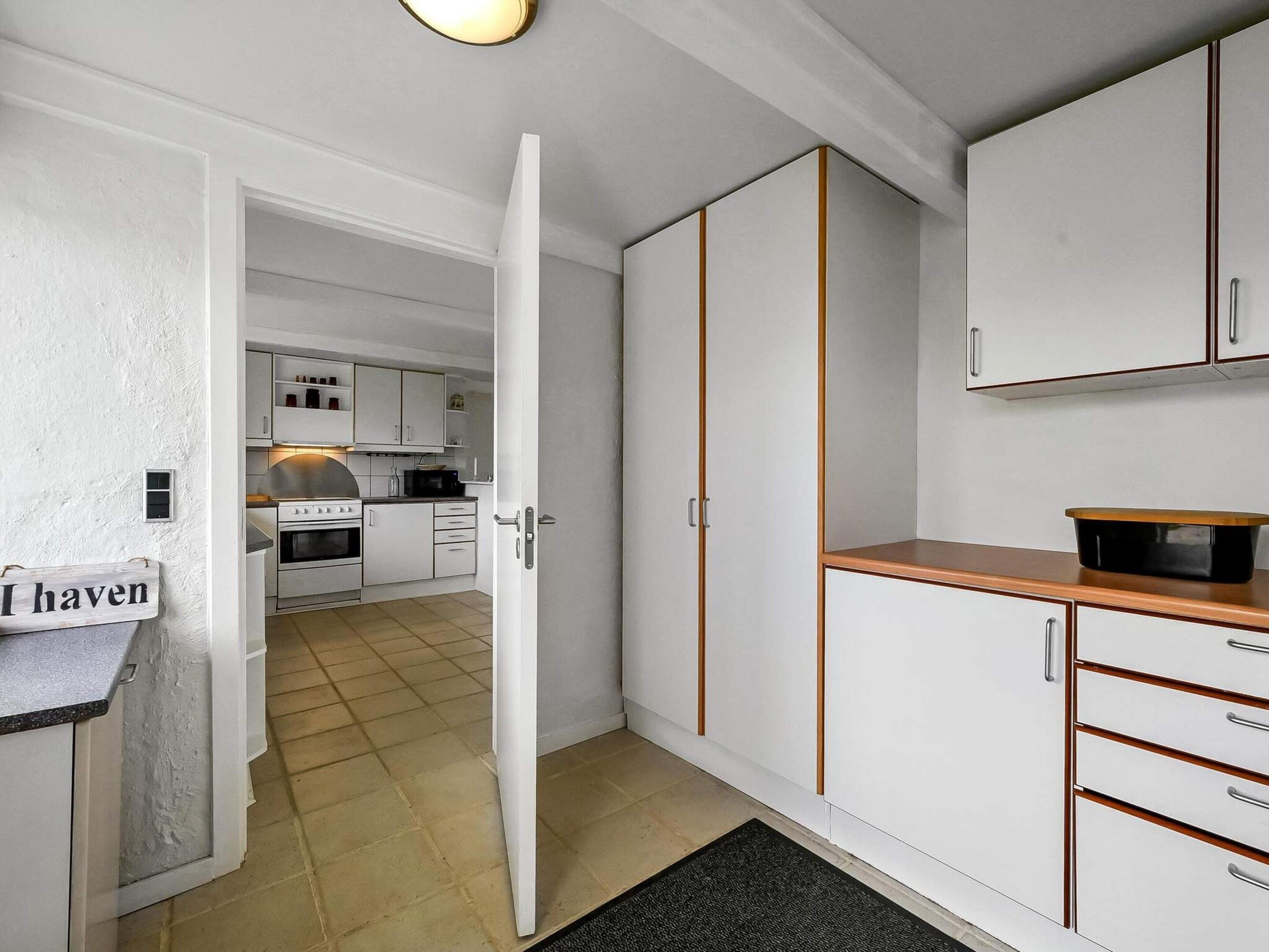 Een kleine keuken met witte kastjes, een houten aanrechtblad en een zwarte pan aan de rechterkant.
