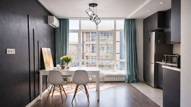A modern kitchen with a dining area, large windows, and a view of buildings.