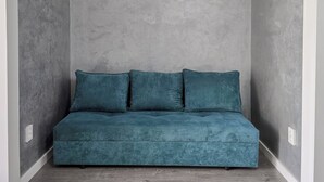 A teal sofa in a corner with grey textured walls and a wooden floor.