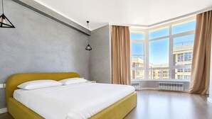 A modern hotel room with a large bed, a view of the city, and a large window.