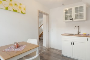 Een kleine keuken met een houten tafel, een witte stoel en een kast met glazen deuren.