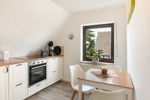 A kitchen with white cabinets, a wooden countertop, a coffee maker, a kettle, and a window with a view of a house and trees.