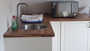 A kitchen with a stainless steel sink, a dish rack, a bottle of dish soap, a toaster, and white cabinets.