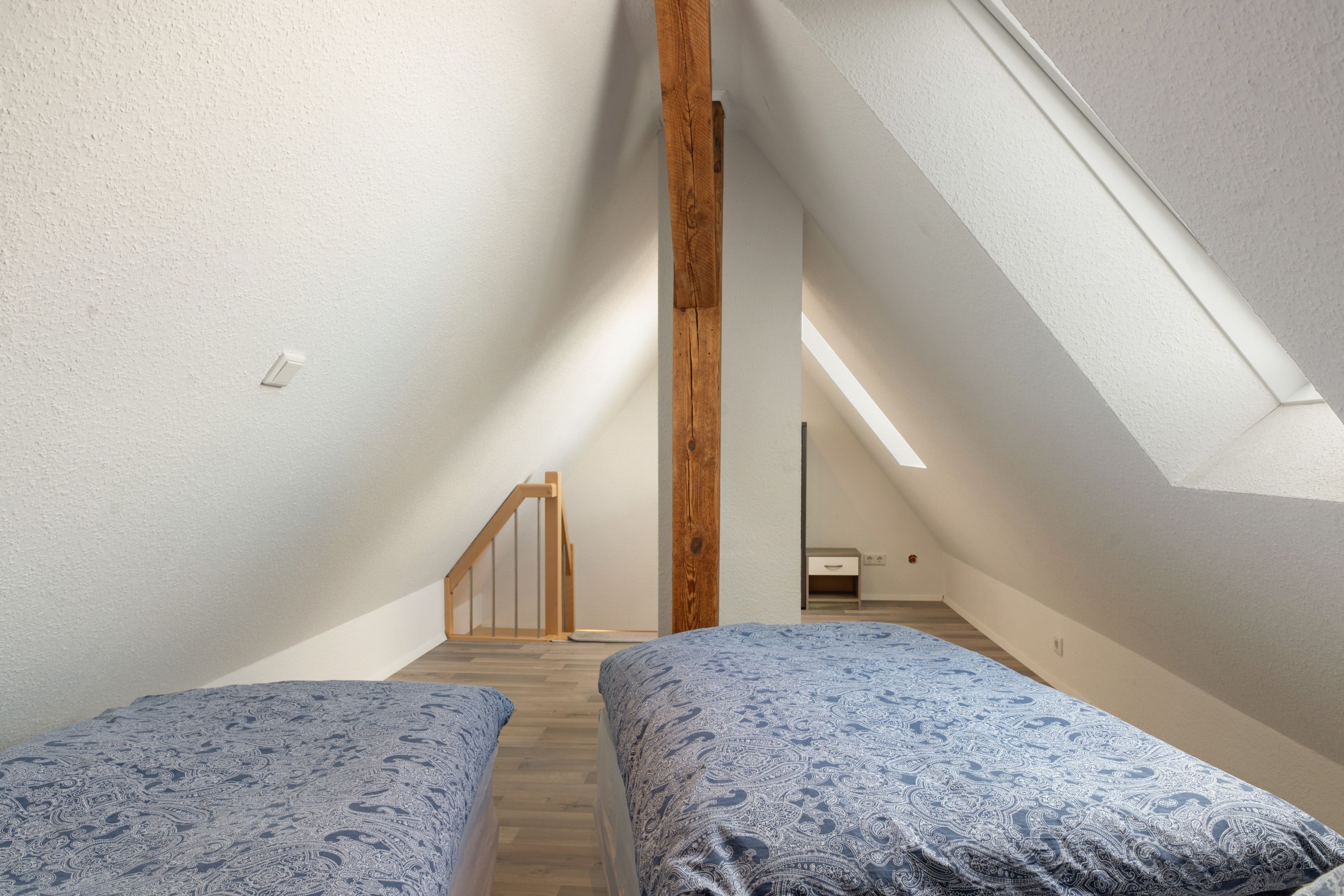 Een kamer met twee bedden, houten balken, een schuine plafond en een dakraam.