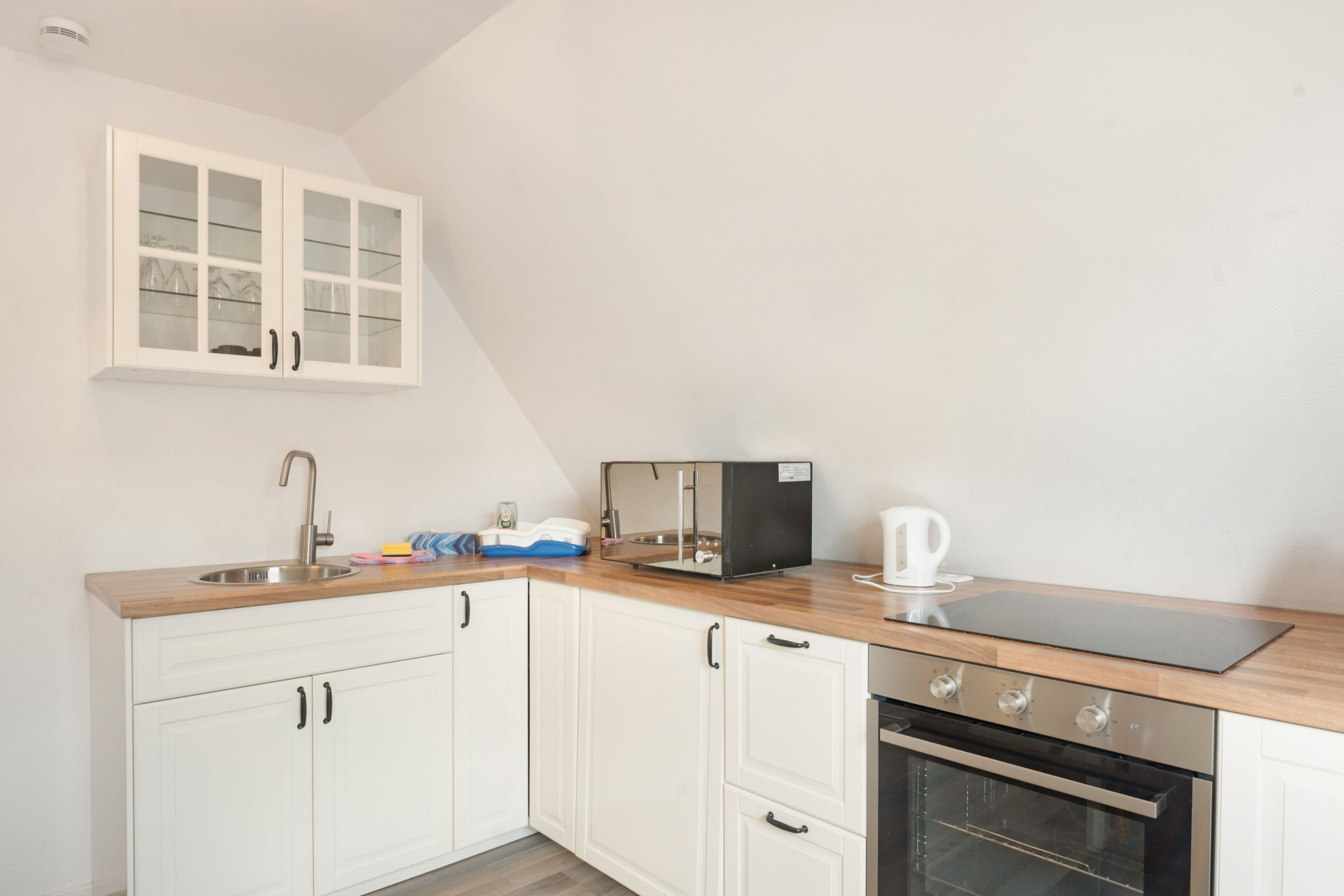 A kitchen with white cabinets, a stainless steel sink, a black coffee maker, and an oven.
