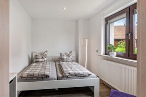 Une petite chambre avec un lit simple, une fenĂȘtre, des murs blancs et un radiateur.