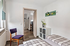 Un dormitorio con una cama, una silla, un armario pequeño y una puerta que da a una cocina.