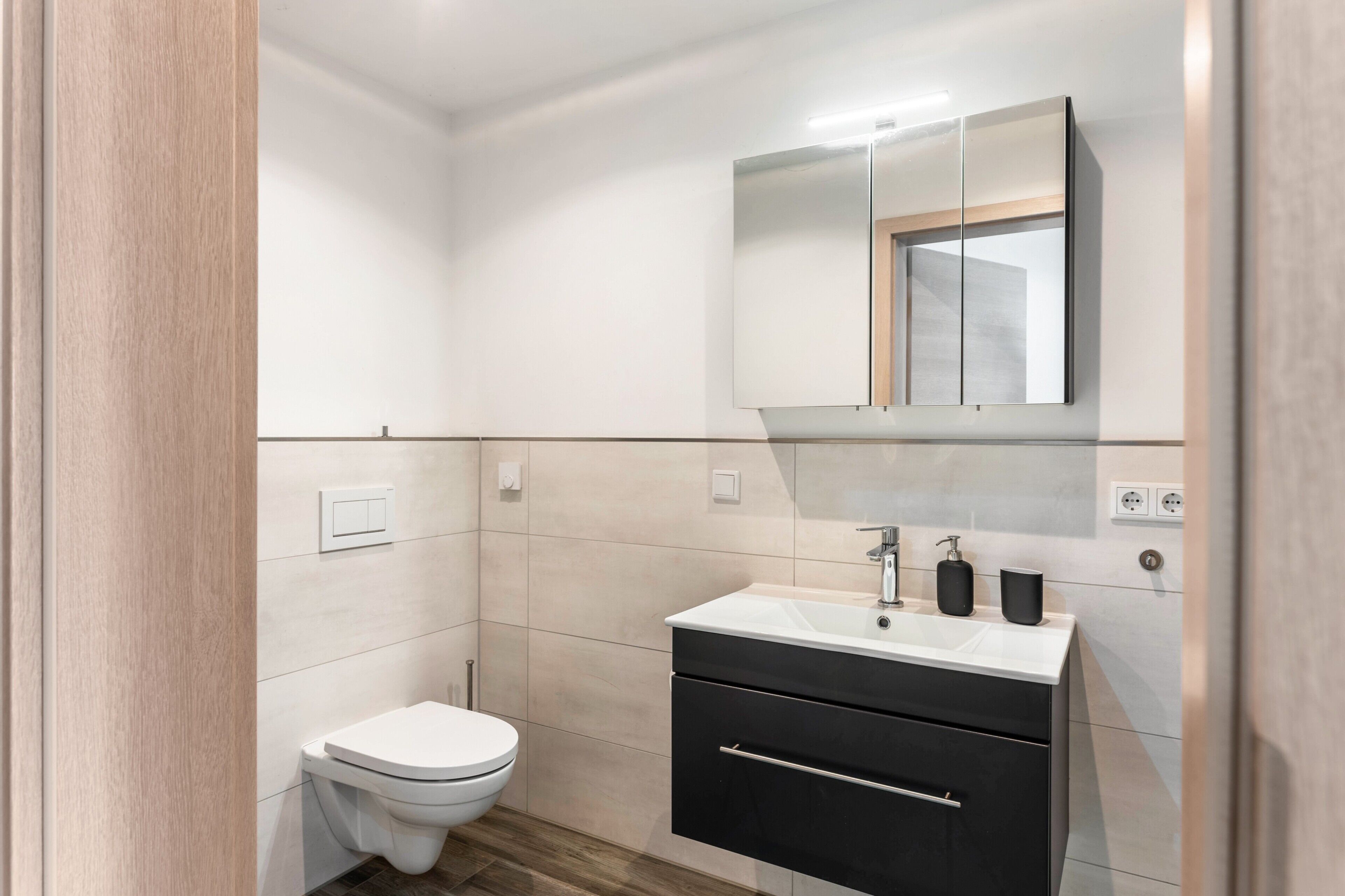 Ein modernes Badezimmer mit Toilette, Waschbecken und einem Spiegel darüber sowie einem schwarzen Schrank.