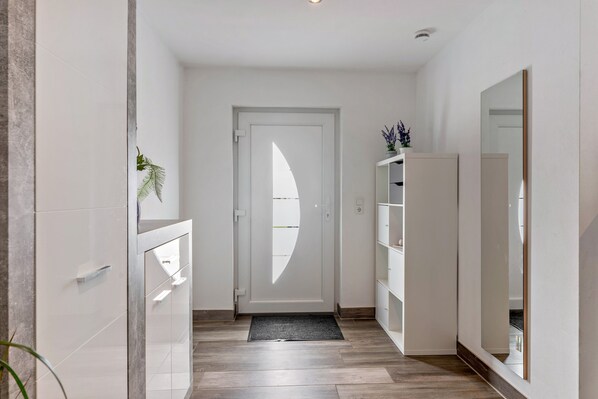 A hallway with a white door, a plant, and a mirror.