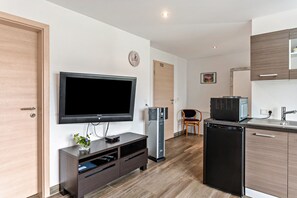 A modern kitchen with a built-in microwave, a refrigerator, and a flat-screen TV mounted on the wall.