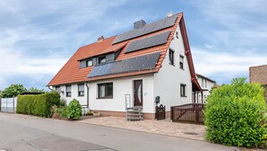 Una casa con techo inclinado, paneles solares, una puerta principal y un pequeño jardín delantero.