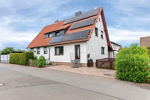 Une maison avec un toit en pente, des panneaux solaires, une porte dâentrĂ©e et un petit jardin devant.