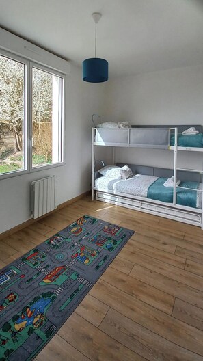 Ein Zimmer mit Etagenbett, Heizkörper, Fenster mit Blick auf Bäume und einem farbenfrohen Teppich.