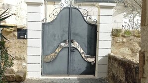 A gated entrance with a metal gate, a stone wall, and a building with a sloped roof. - Family home for a quiet stay close to all amenities! (Montrichard Val de Cher)