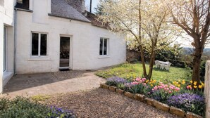A white building with a gravel driveway, a garden with colorful flowers, and a tree with white blossoms. - Family home for a quiet stay close to all amenities! (Montrichard Val de Cher)