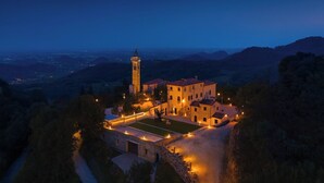 Un edificio histórico con una torre, rodeado por un patio bien iluminado y con vistas a un valle.
