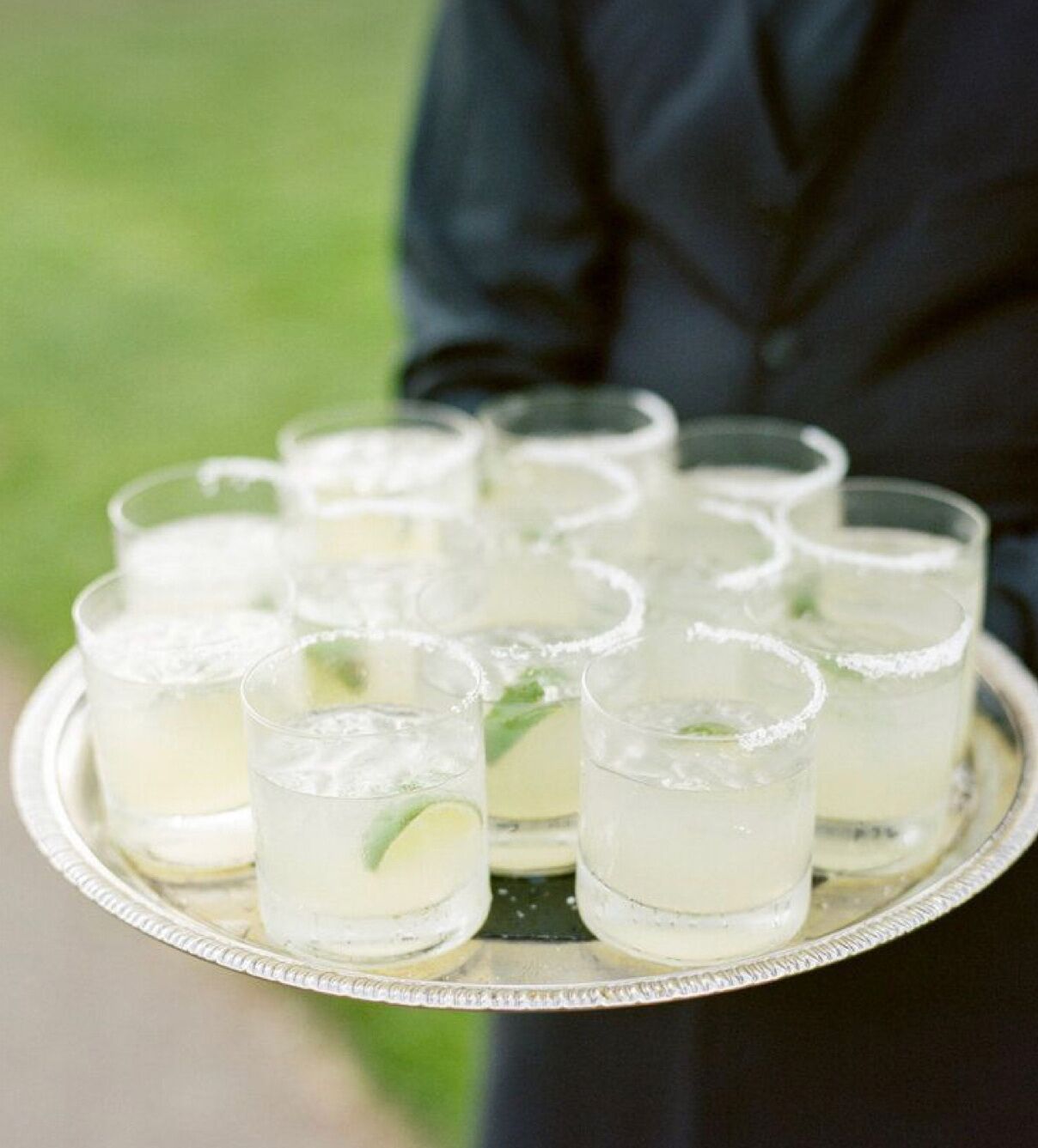 A tray with multiple glasses of a clear beverage, garnished with lime, held by a person.