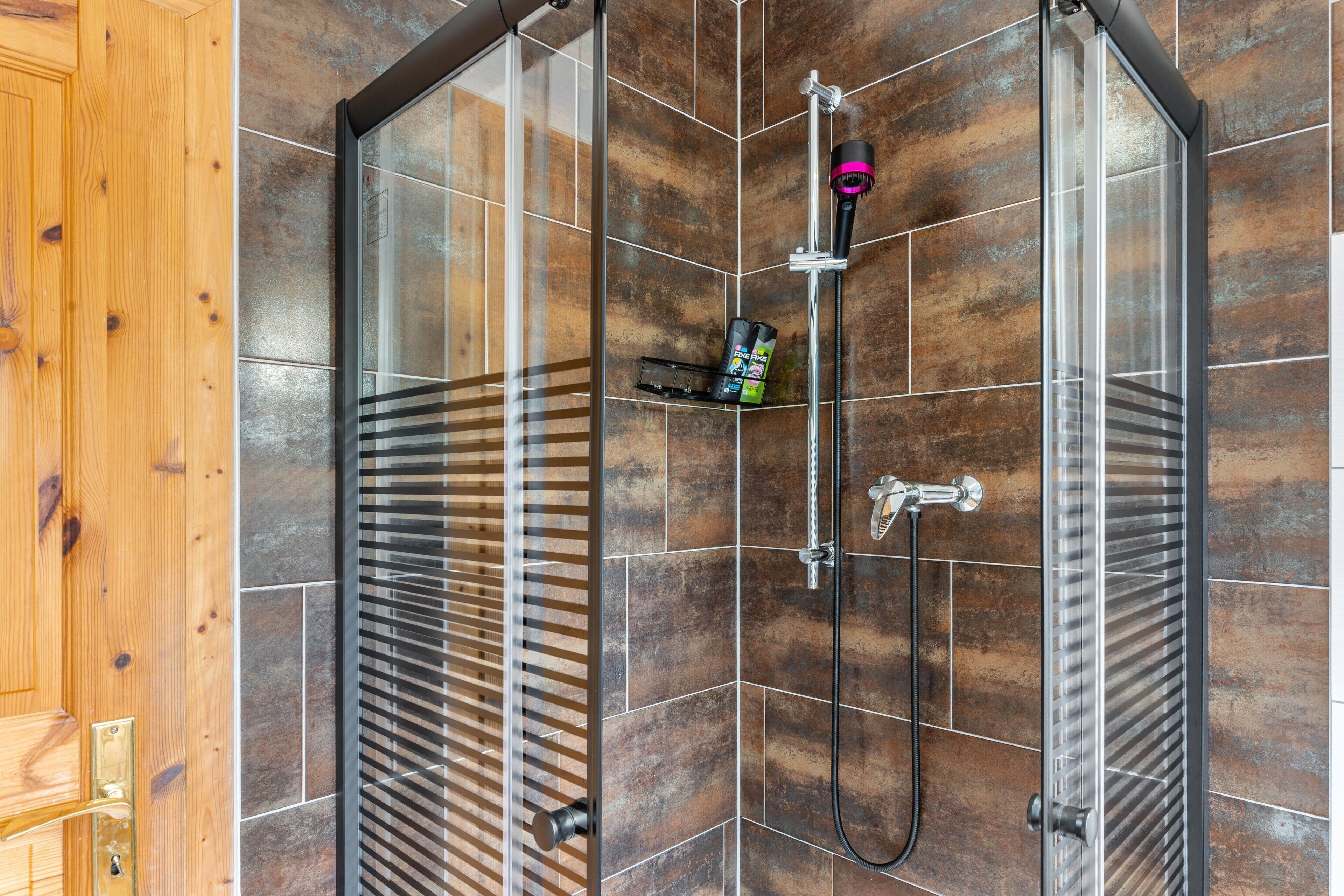 A shower enclosure with a glass door, a handheld showerhead, and a handheld shower attachment.