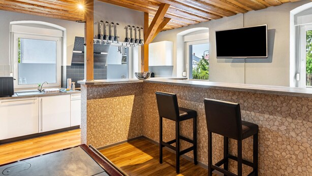Une cuisine avec un mur recouvert de pierres apparentes, des poutres en bois au plafond, un bar intégré avec deux tabourets et un téléviseur à écran plat fixé au mur.
