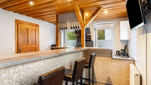Une cuisine avec un mur en pierre, un plafond en bois et un coin bar avec des tabourets.