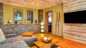 Une pièce chaleureuse avec un mur en pierre, un plafond en bois, un canapé, une table basse et des paires de skis appuyés contre le mur.