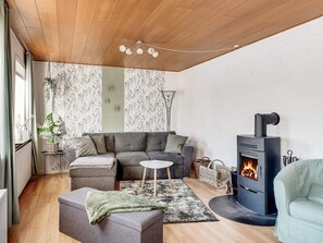 A cozy living room with a sectional sofa, a small round table, a fireplace, and a green ottoman. - 4 Star Holiday Home in Lokken (Lokken)