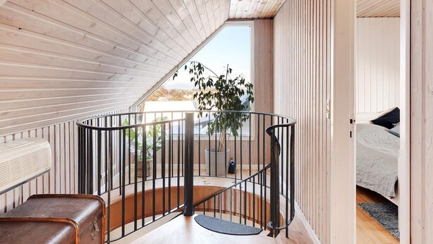 A loft bedroom with a sloped ceiling, a spiral staircase, a bed, and a view of the outdoors. - 4 Star Holiday Home in Lokken (Lokken)