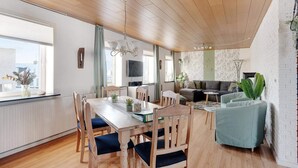 A spacious living area with a wooden dining table, chairs, a sofa, and a TV. - 4 Star Holiday Home in Lokken (Lokken)