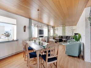 A spacious living area with a wooden dining table, chairs, a sofa, and a TV. - 4 Star Holiday Home in Lokken (Lokken)