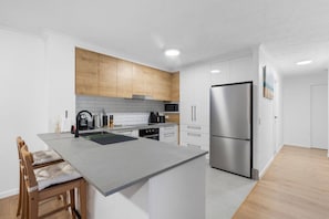 Una cocina moderna con una isla central, armarios de madera, paredes blancas y un refrigerador de acero inoxidable.