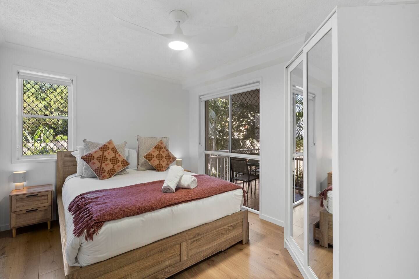 A bedroom with a bed, two nightstands, a ceiling fan, and large windows.